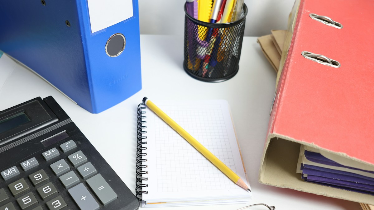 Binders, a notebook, a calculator and reading glasses on a desk, ready for gathering the documents a sole proprietor needs to apply