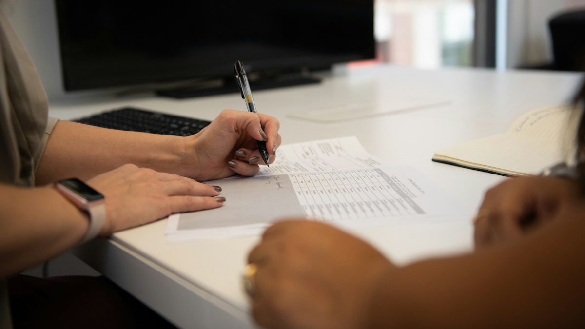 Business owner tracing line items on a printed merchant processing statement with a pen at a desk