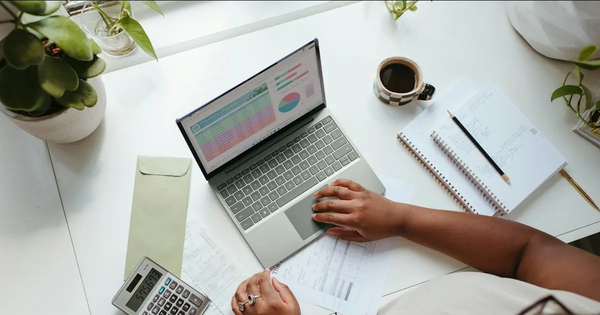 Business owner comparing credit card processing fees on a laptop spreadsheet with a calculator and printed merchant statements