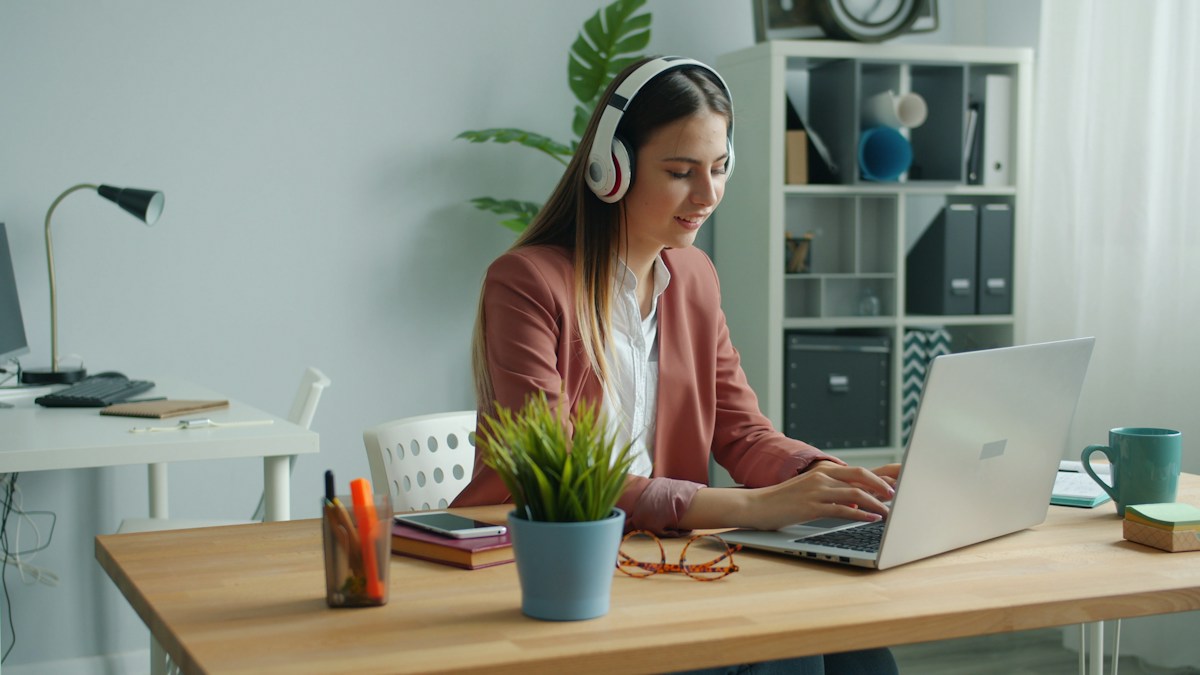Freelancer wearing headphones working on a laptop at her home office desk, a typical one-person business that bills clients by card