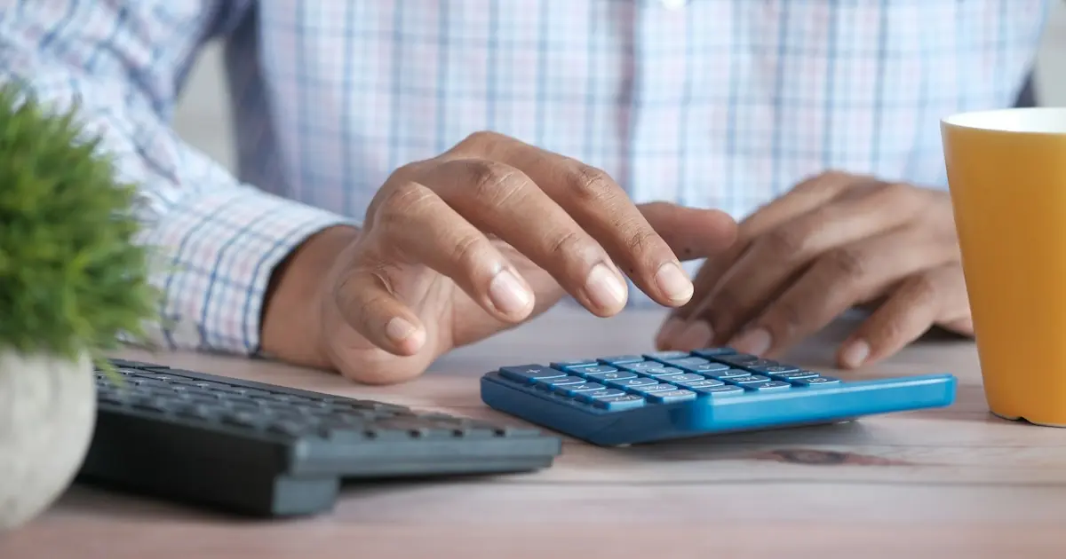 Business owner using a calculator at a desk to work out interchange-plus pricing and card processing fees