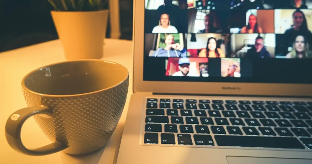 Laptop on a desk showing an online coaching video call next to a coffee mug, illustrating a merchant account for a coaching business