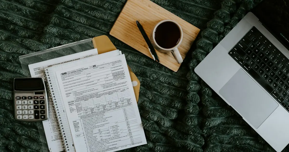 Tax forms, a calculator, coffee and a laptop on a desk while preparing a merchant account for sole proprietors application