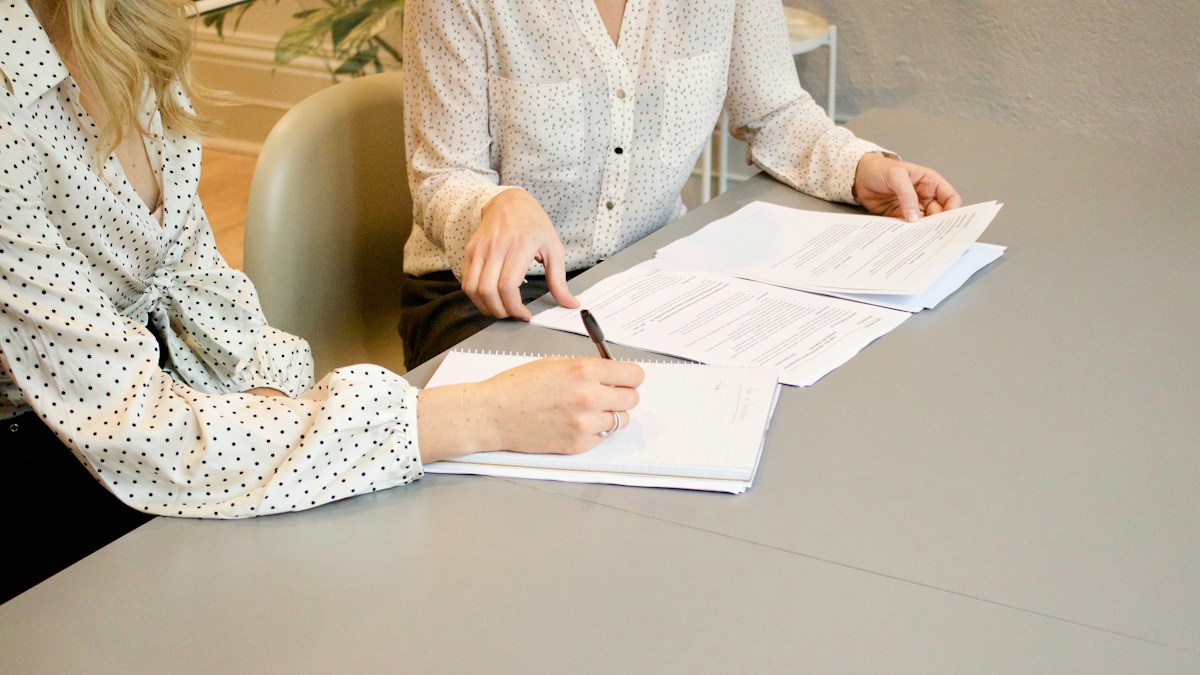 Two people at a table reviewing printed processing statements while preparing a merchant account application