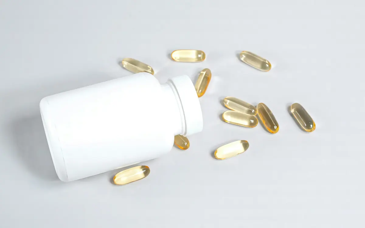 Supplement softgel capsules spilling from a white bottle