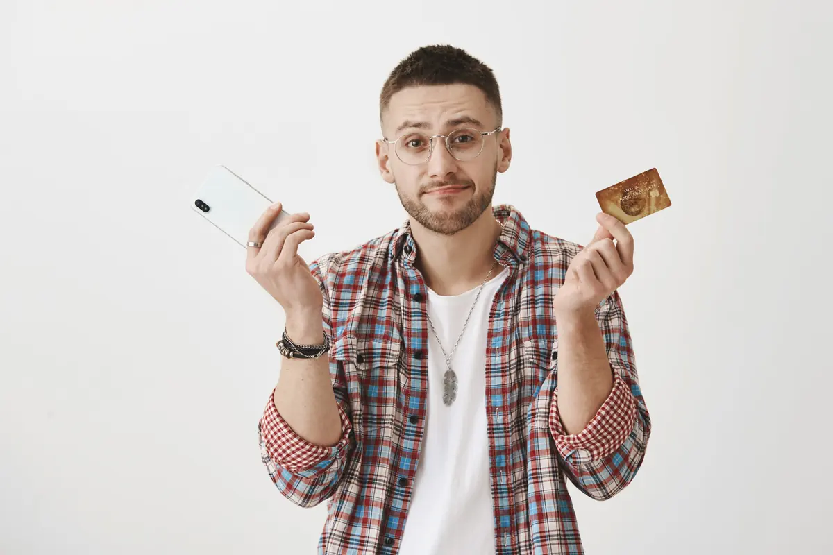 Surprised young man with glasses holding a phone and a payment card